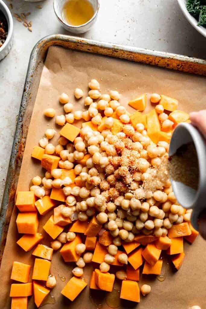 Seasoning being added over sweet potatoes and chickpeas on a baking sheet