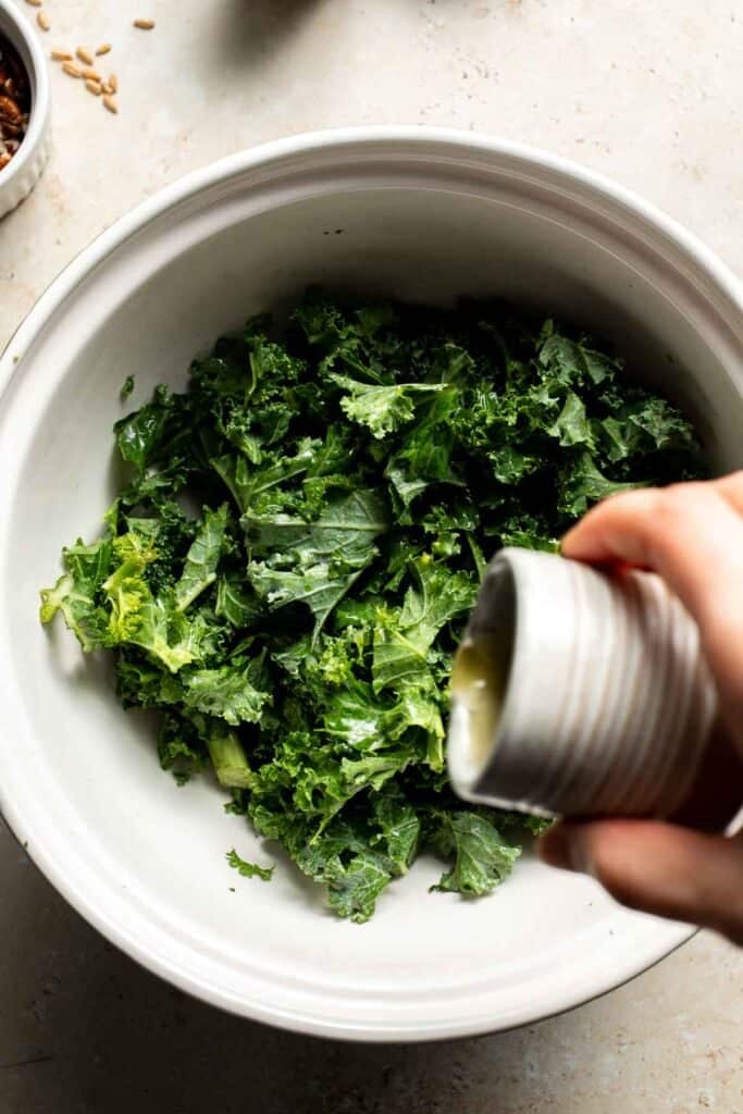 Olive oil being poured into a large bowl of kale
