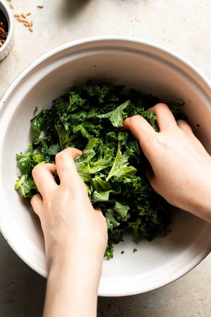 Hands massaging kale with olive oil and salt in a bowl