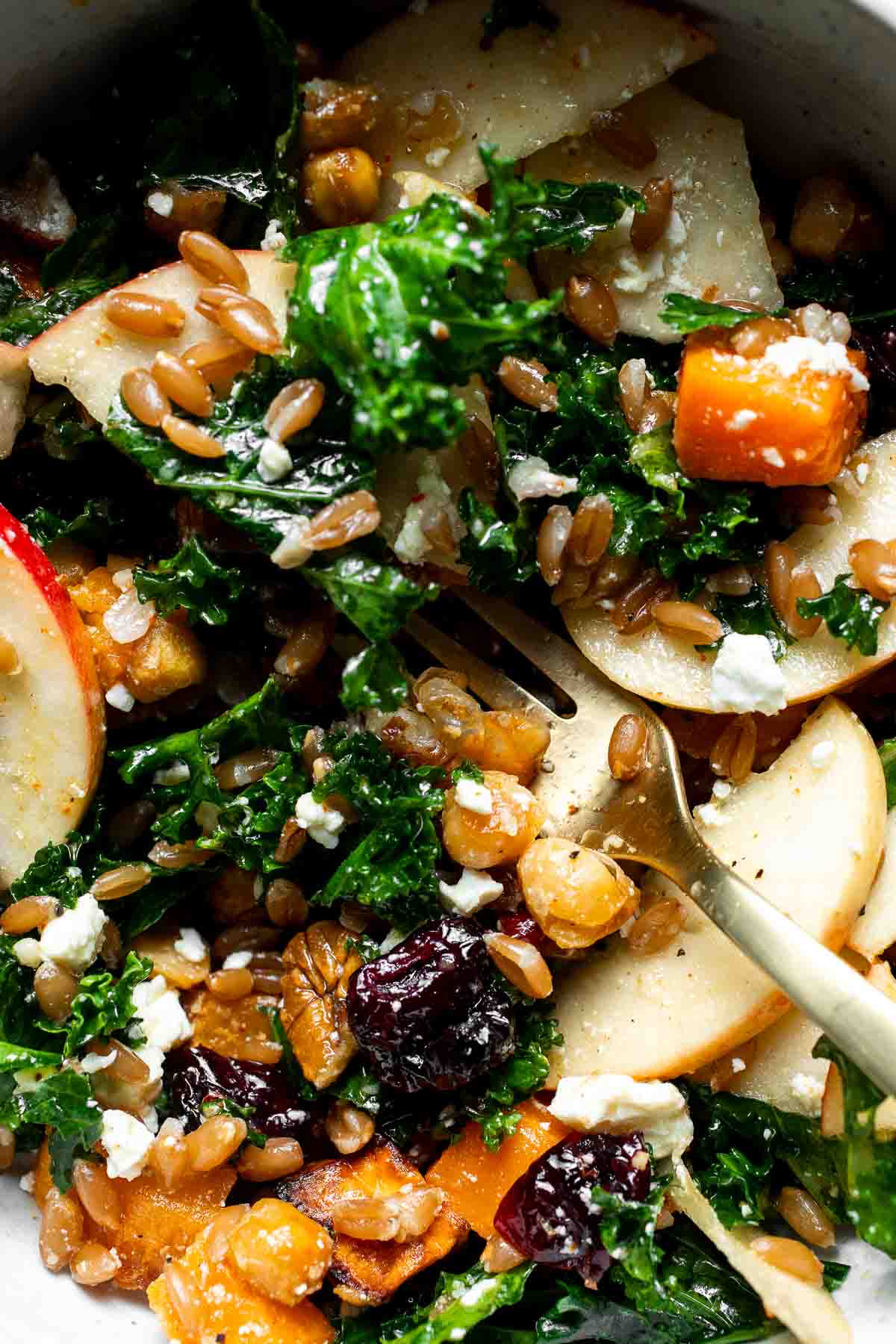 Close-up overhead view of a harvest grain bowl showing farro, kale, apple, and feta