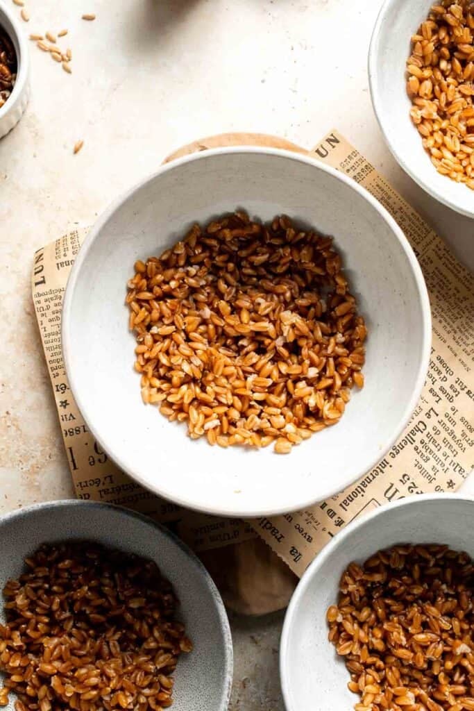 A bowl of cooked farro next to bowls of other harvest grain bowl ingredients