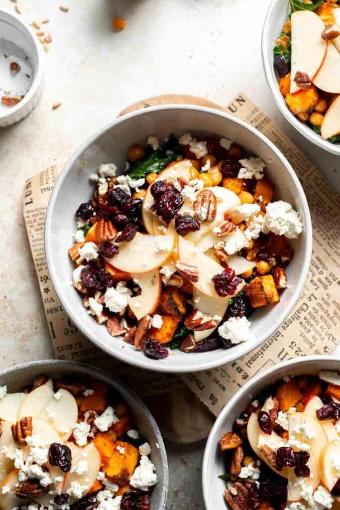 Feta cheese, pecans, and dried cranberries being sprinkled over a harvest grain bowl