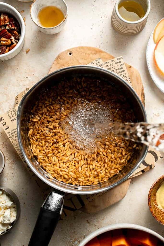 Water being poured to a saucepan of farro