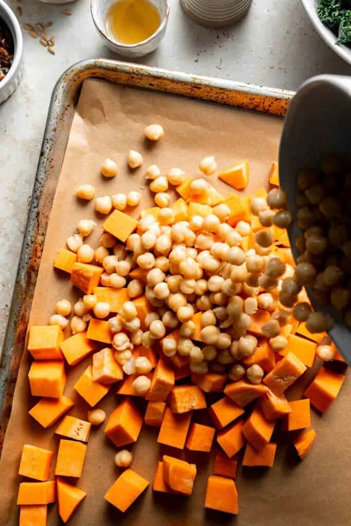 Diced sweet potatoes and chickpeas being added onto a baking sheet