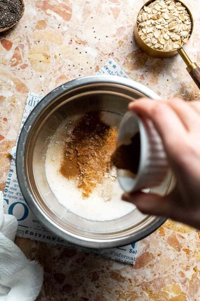 Cinnamon being sprinkled into a bowl of protein oat mixture