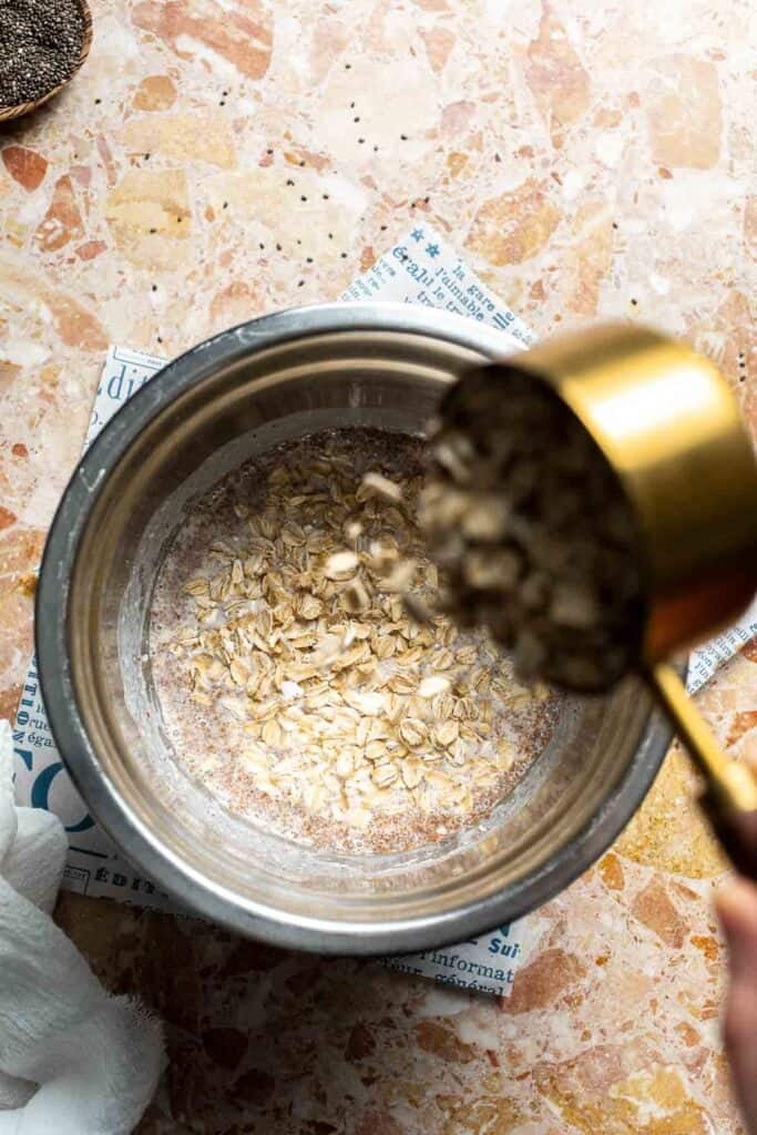 Rolled oats being poured into a bowl of whisked wet ingredients