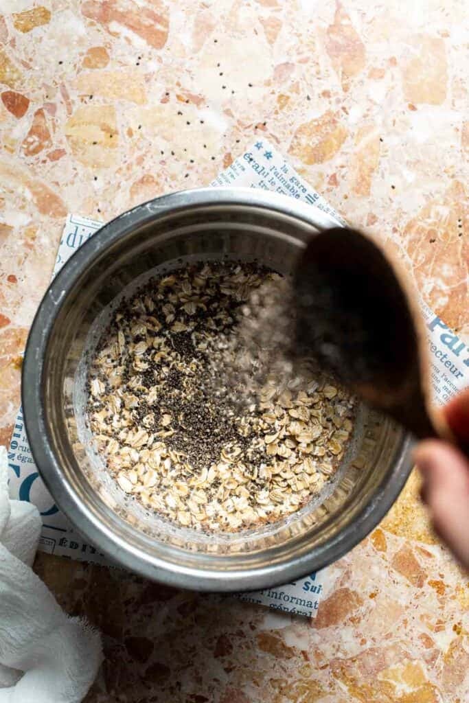 Chia seeds being poured into a bowl of oats and wet ingredients