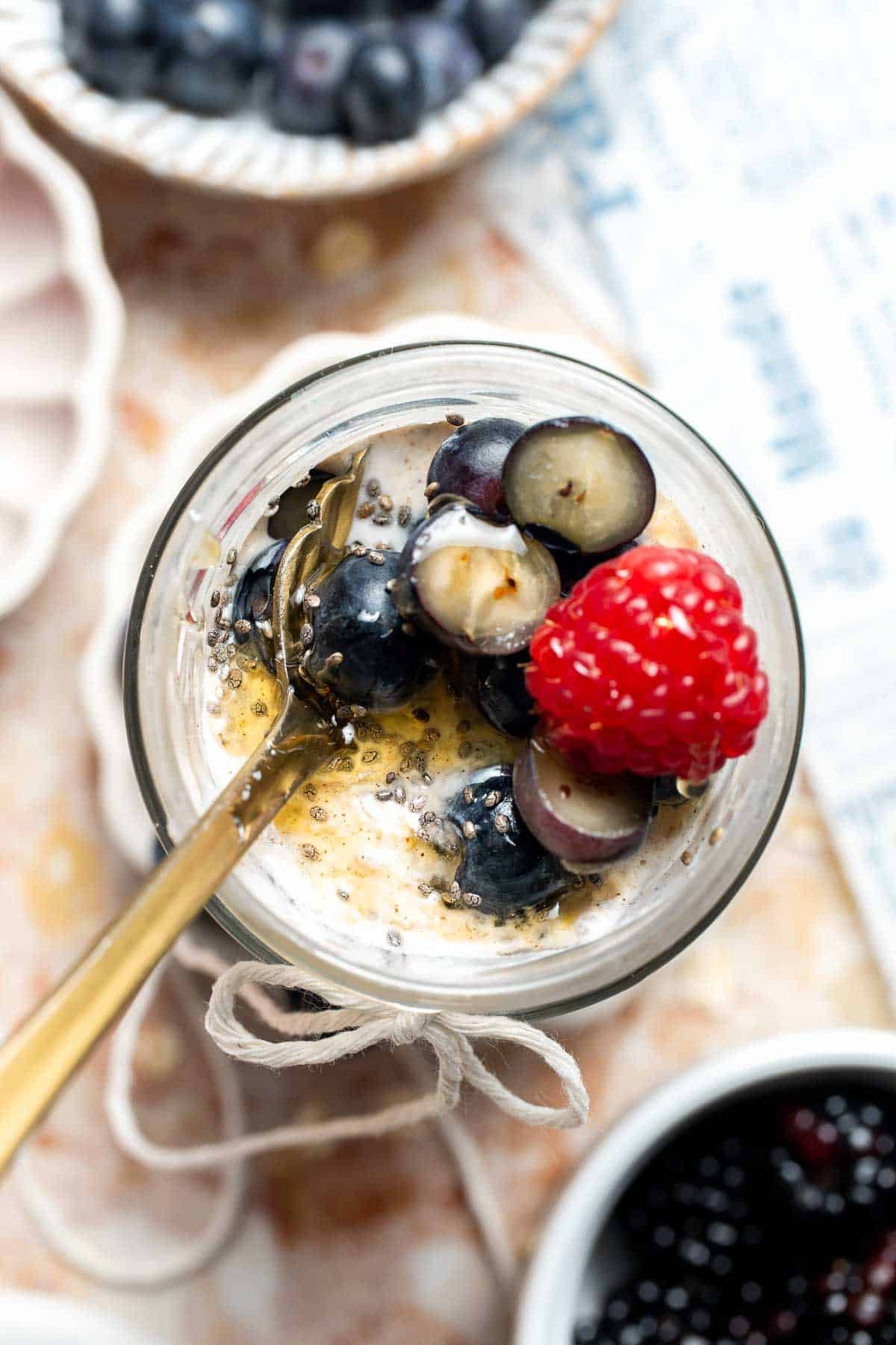 Close up view of high protein overnight oats topped with blueberries and raspberries and a drizzle of honey, served with a spoon