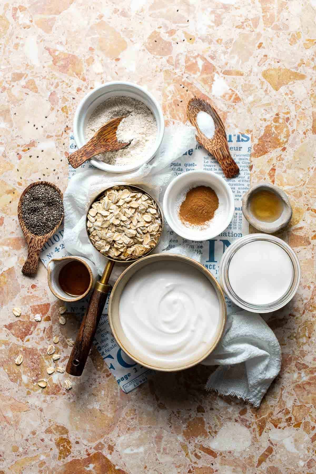 Ingredients for high protein overnight oats including yogurt, oats, protein powder, and honey arranged on a marble surface