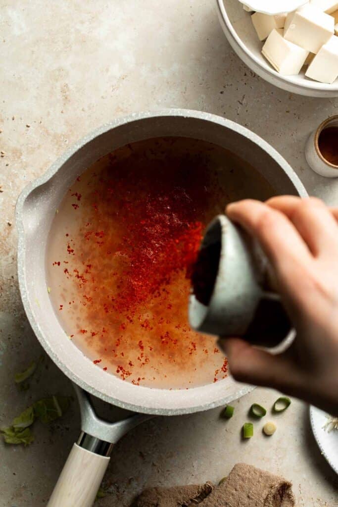 Gochugaru being poured into a pot of simmering broth