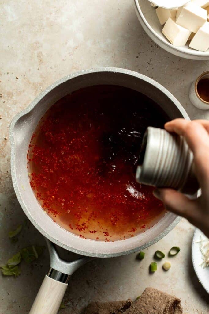 Soy sauce being poured into a pot of seasoned broth