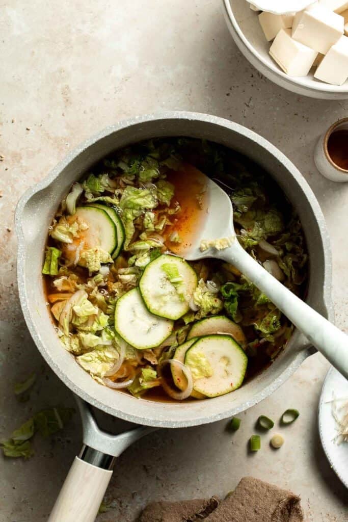 Zucchini and cabbage being stirred into broth in a pot