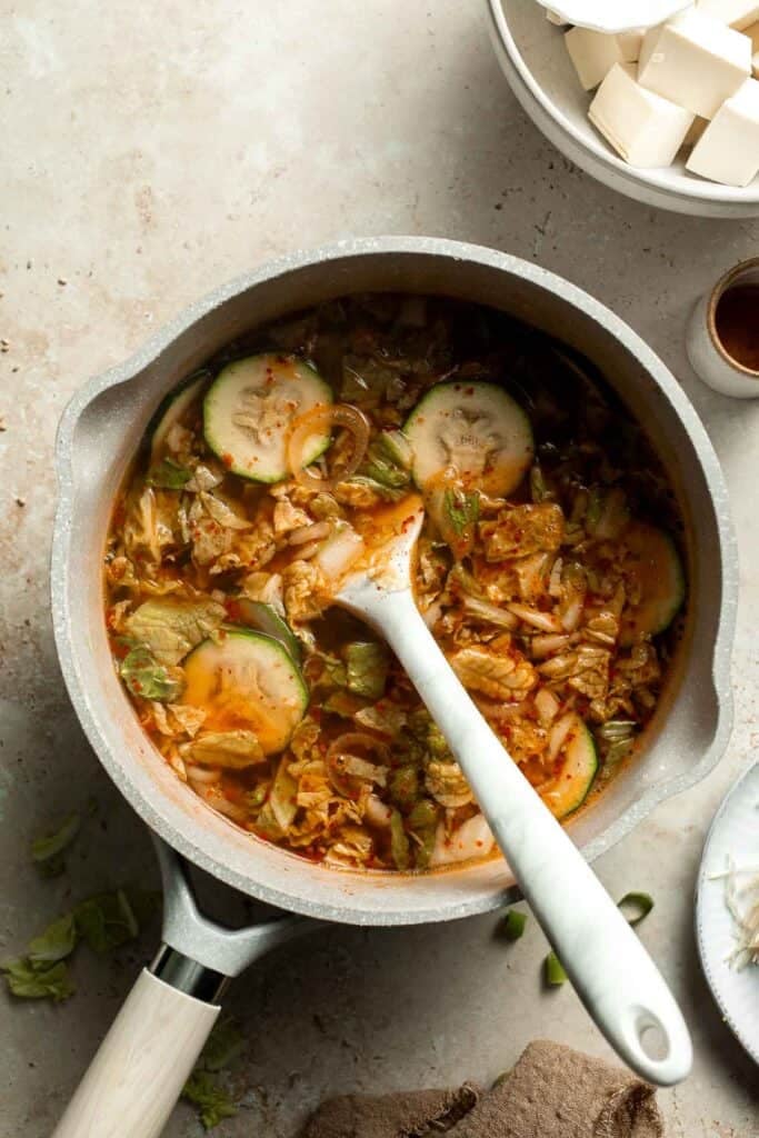 Vegetables simmering in broth with a spoon
