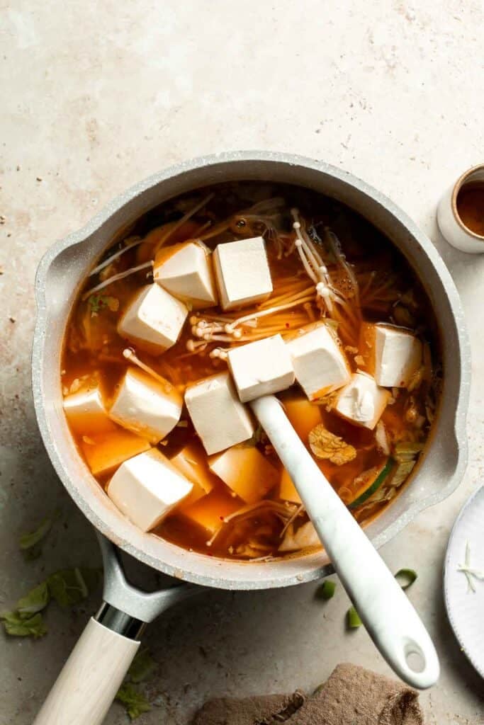 Tofu being spooned into a pot of simmering soup