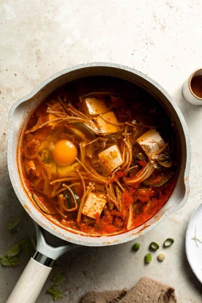 An egg cracked into a pot of simmering Korean tofu soup