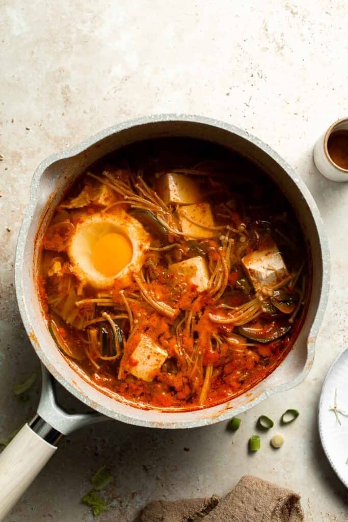 Overhead view of Korean tofu soup with tofu, poached egg, and vegetables in a pot