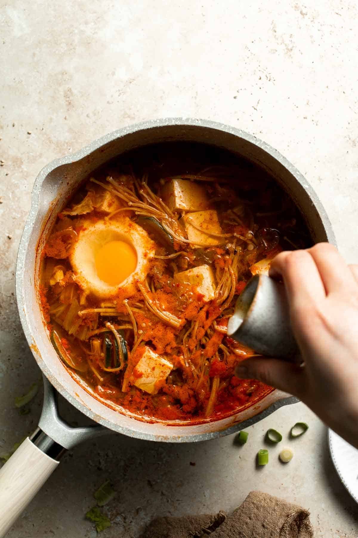 Adding a drizzle of sesame oil to a pot of Korean tofu soup