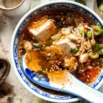 Korean tofu soup served in a blue and white bowl with sesame seeds and green onion