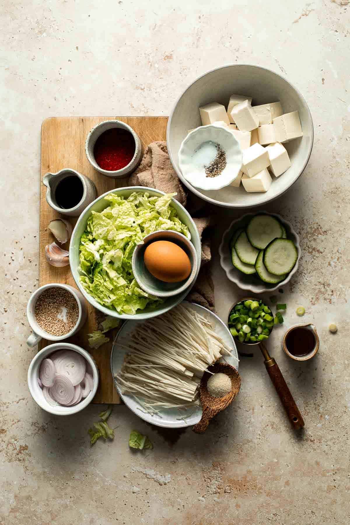 Ingredients for Korean tofu soup including tofu, garlic, zucchini, and egg arranged on a cutting board
