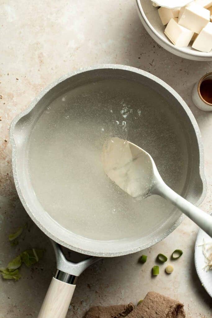 Dashi powder being stirred into water with a spoon in a pot
