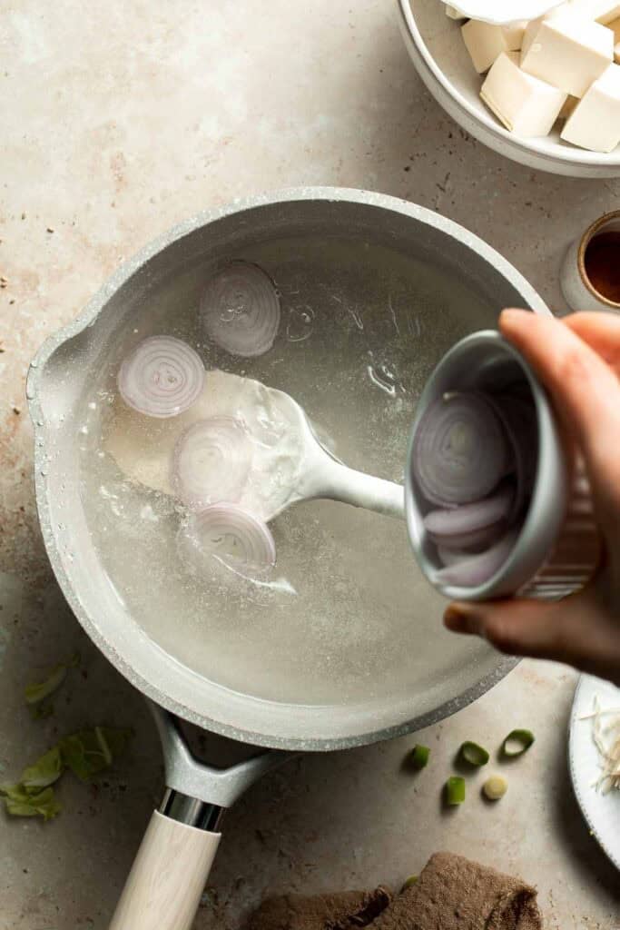 Shallot being added to simmering broth in a pot