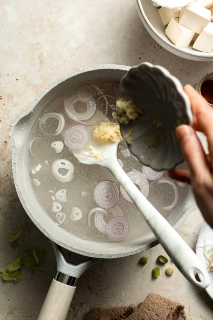 Garlic being added to simmering broth in a pot