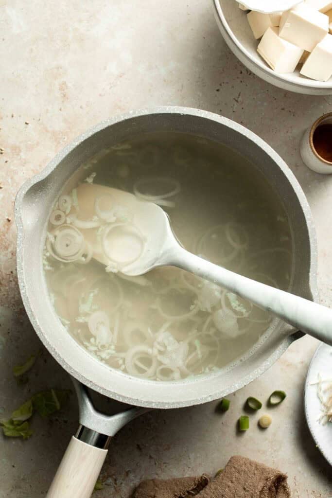 Broth being stirred with a spoon in a pot