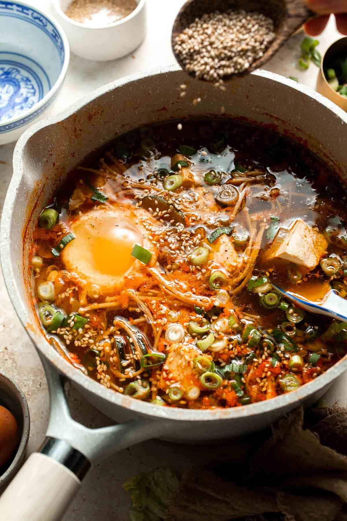 Sesame seeds being sprinkled into a pot of finished Korean tofu soup