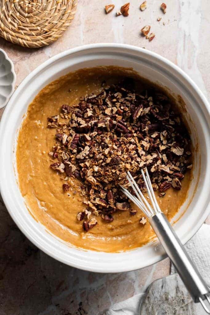 Toasted pecans being folded into muffin batter in a bowl