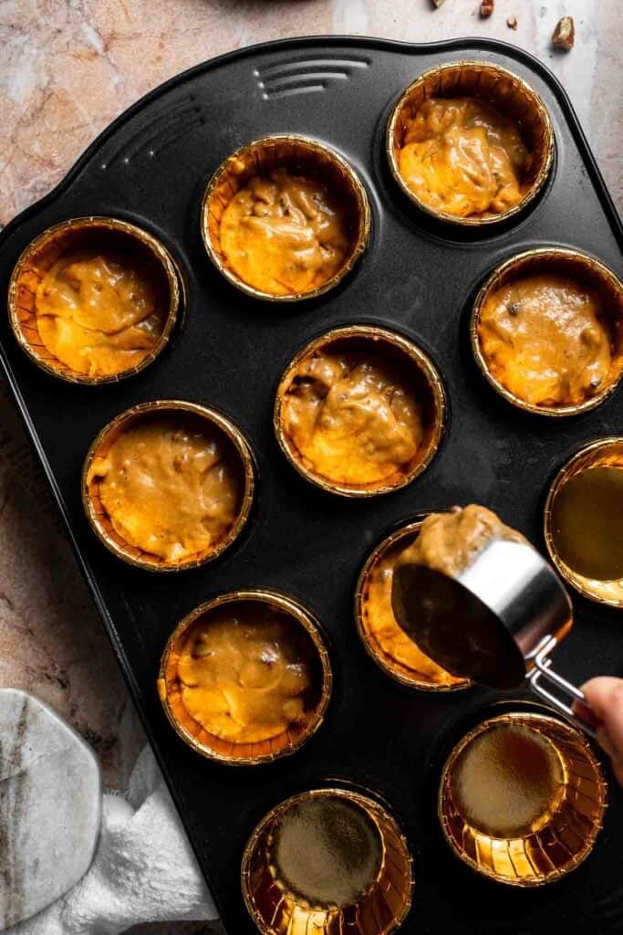 Muffin batter being scooped into a lined muffin pan