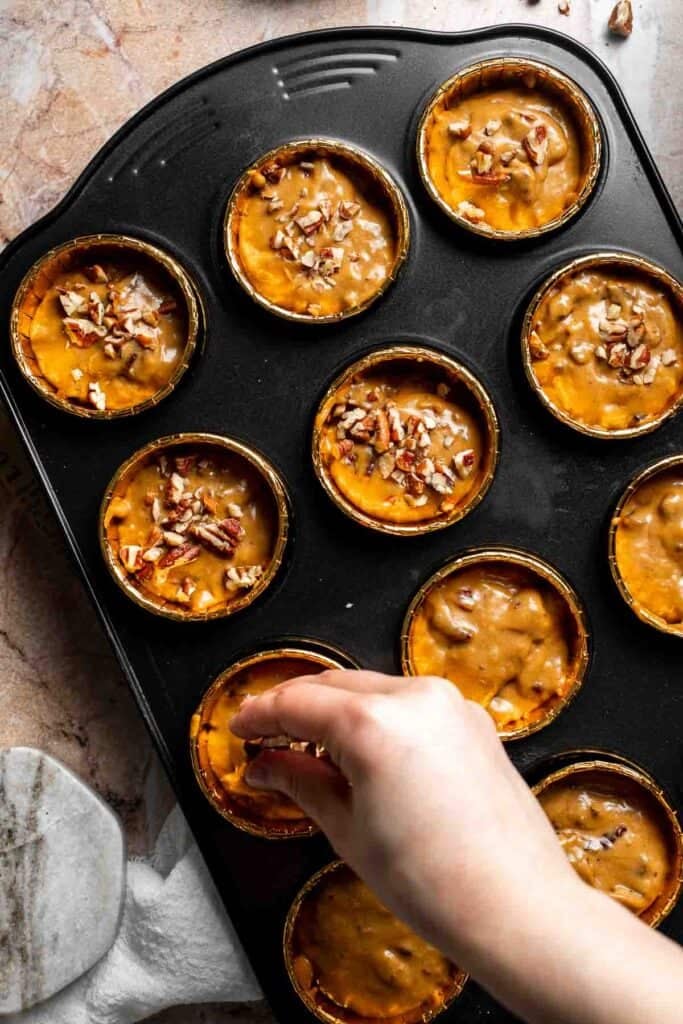Chopped pecans being sprinkled over unbaked muffin batter