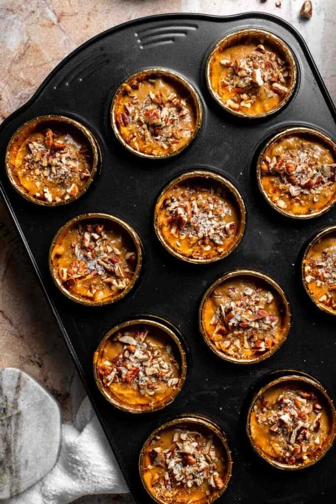 Unbaked muffins topped with chopped pecans and course sugar in a muffin pan