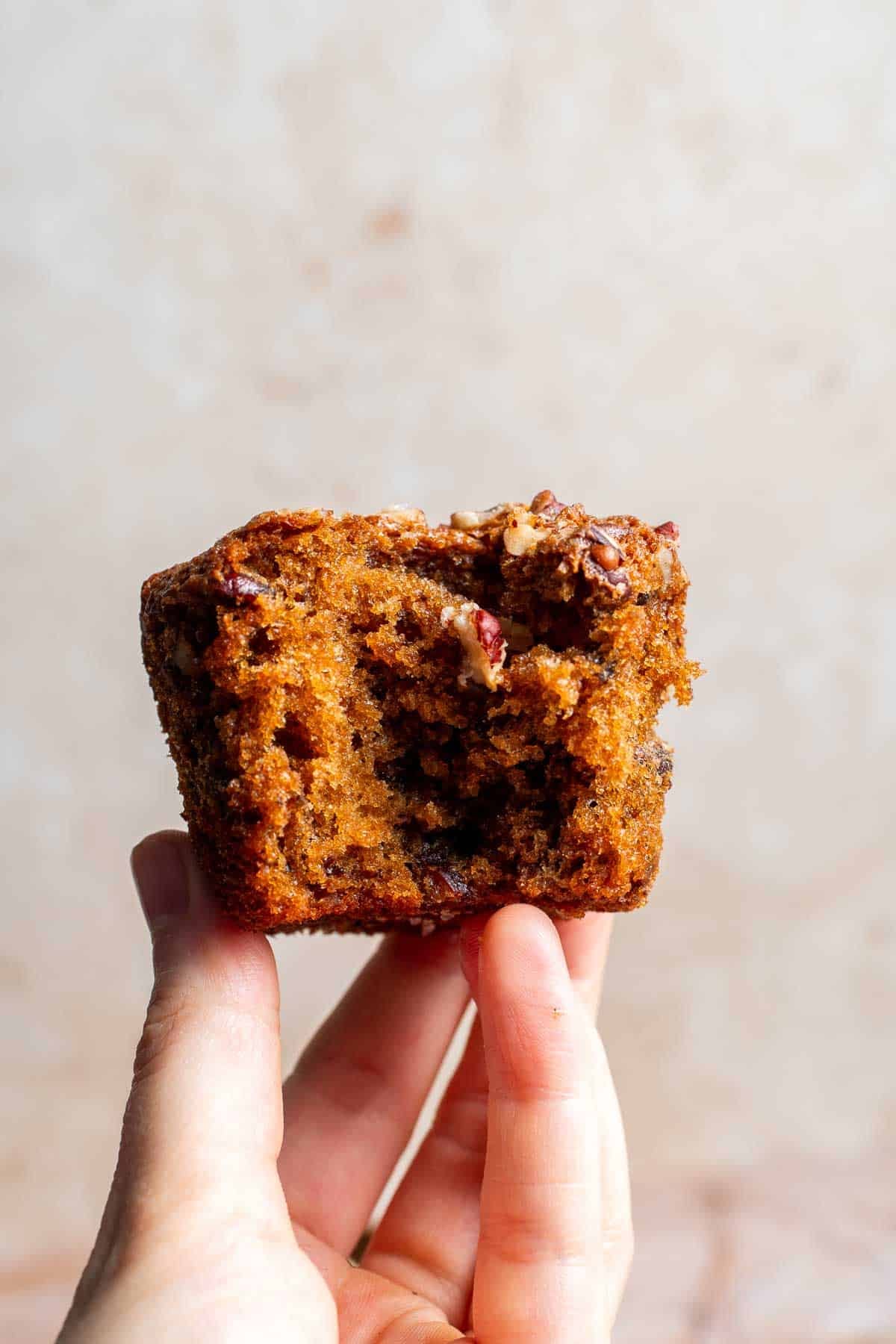 A hand holding half of a pecan pie muffin, showing the moist interior
