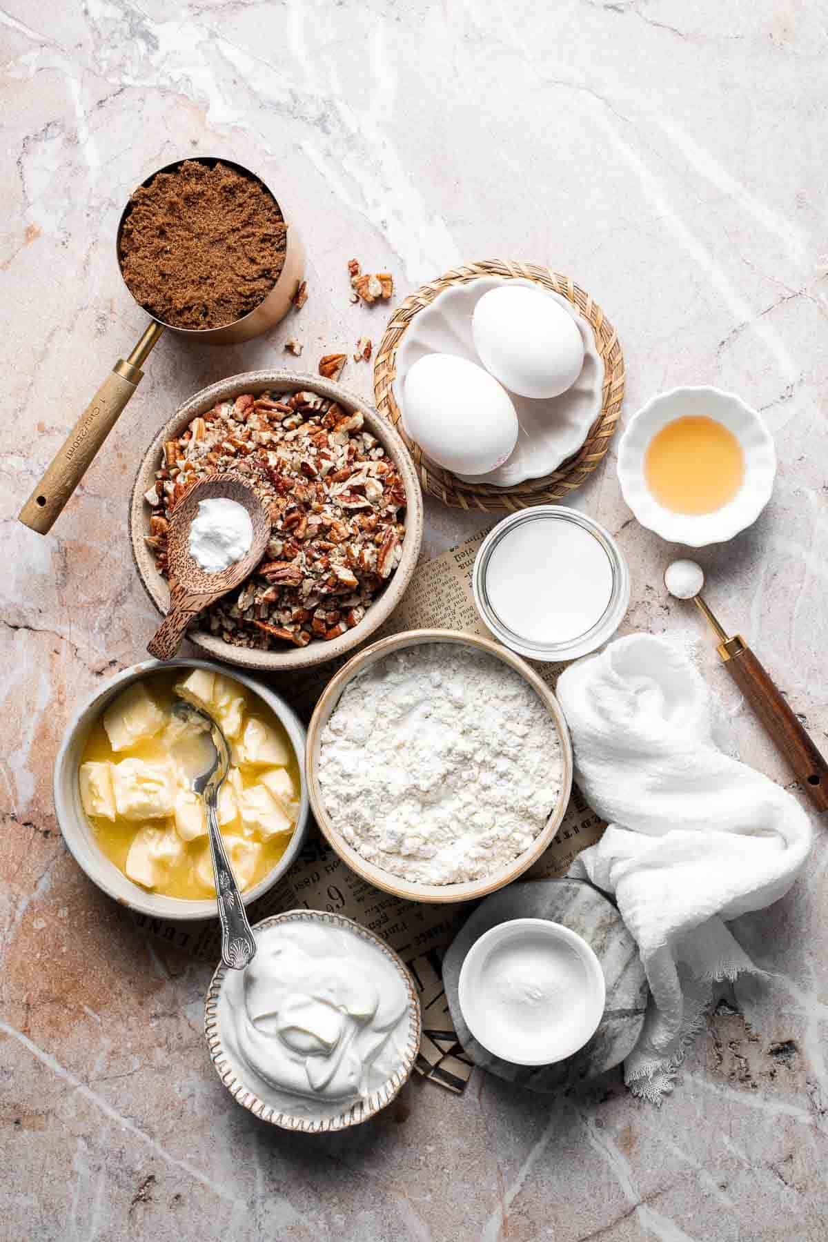 Ingredients for pecan pie muffins including pecans, brown sugar, butter, and flour arranged on a table