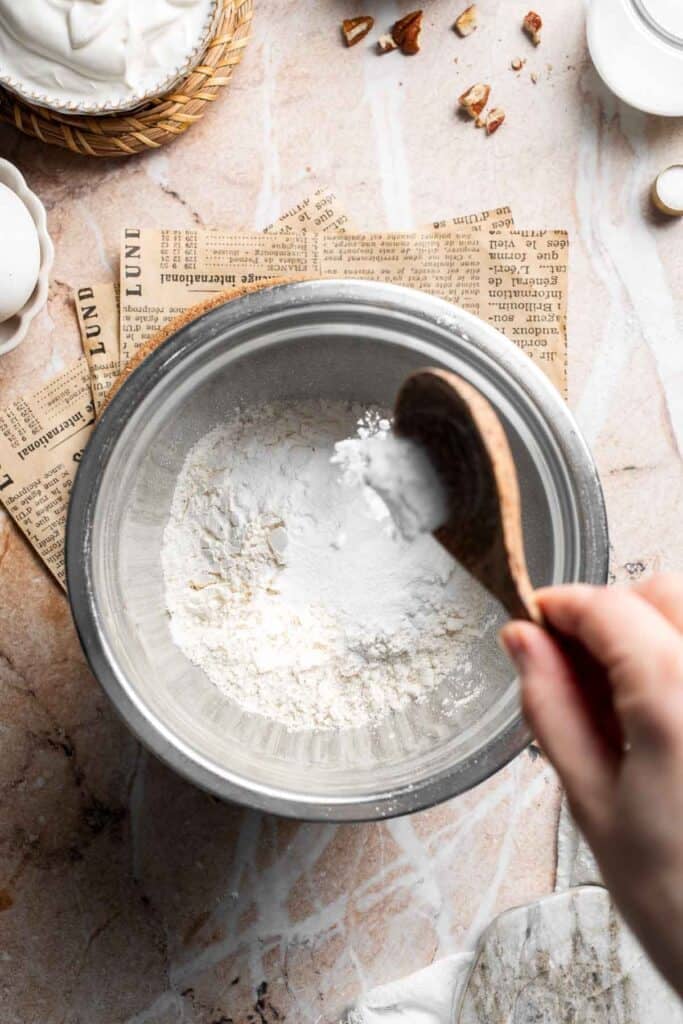 Baking powder being added to a bowl of flour
