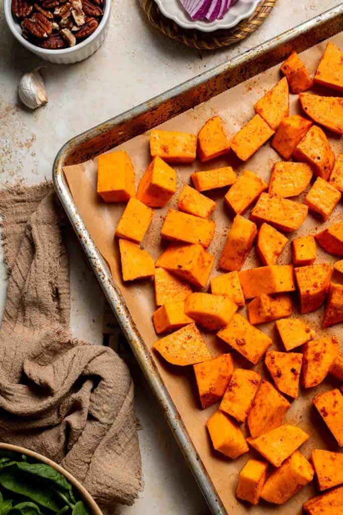 Seasoned sweet potatoes spread on a parchment-lined baking sheet before roasting