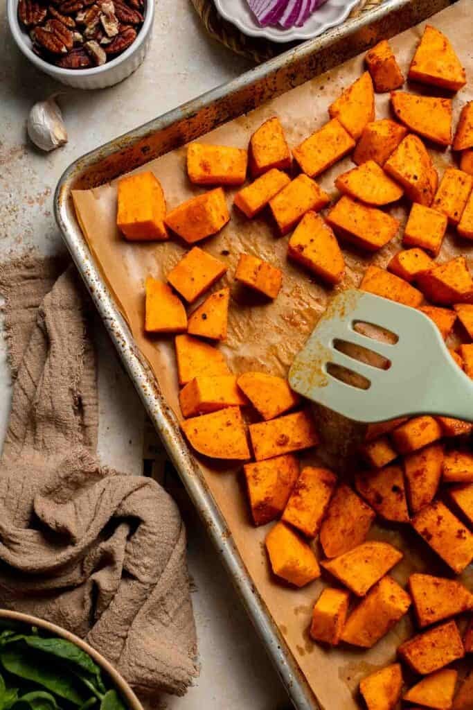 Roasted sweet potatoes being flipped on a baking sheet with a spatula