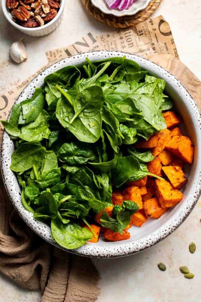 Baby spinach and roasted sweet potatoes combined in a large bowl
