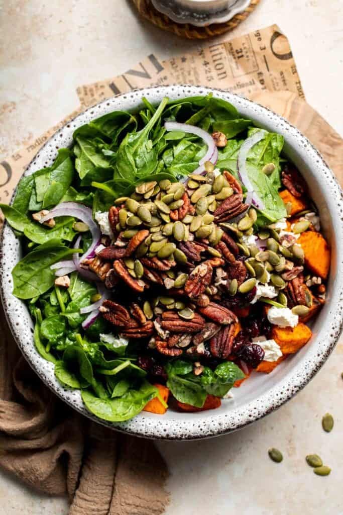 Spinach, roasted sweet potatoes, feta, and pecans combined in a salad bowl