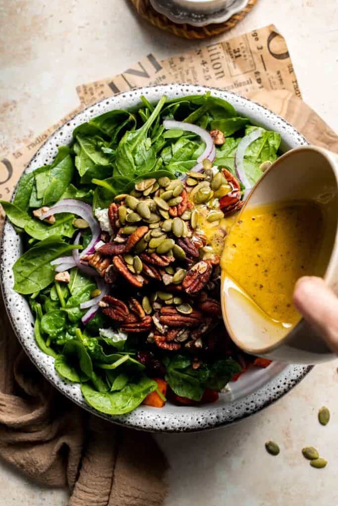 Dressing being poured over a bowl of roasted sweet potato salad
