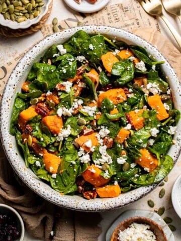 Roasted Sweet Potato Salad with Spinach served in a large bowl with caramelized sweet potatoes, feta, pecans, and cranberries in a maple Dijon dressing