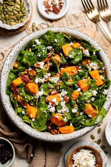 Roasted Sweet Potato Salad with Spinach served in a large bowl with caramelized sweet potatoes, feta, pecans, and cranberries in a maple Dijon dressing