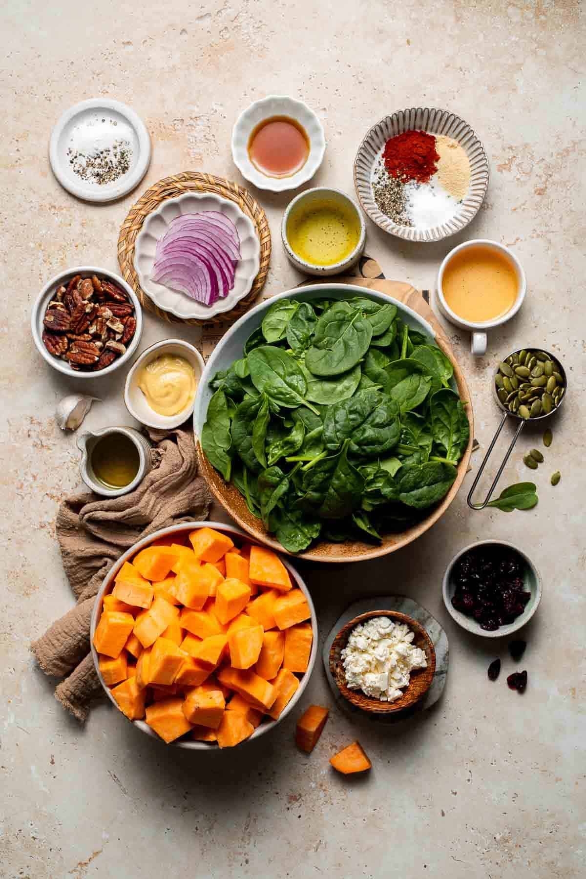 Ingredients for roasted sweet potato salad including spinach, sweet potatoes, feta, and pecans arranged in bowls