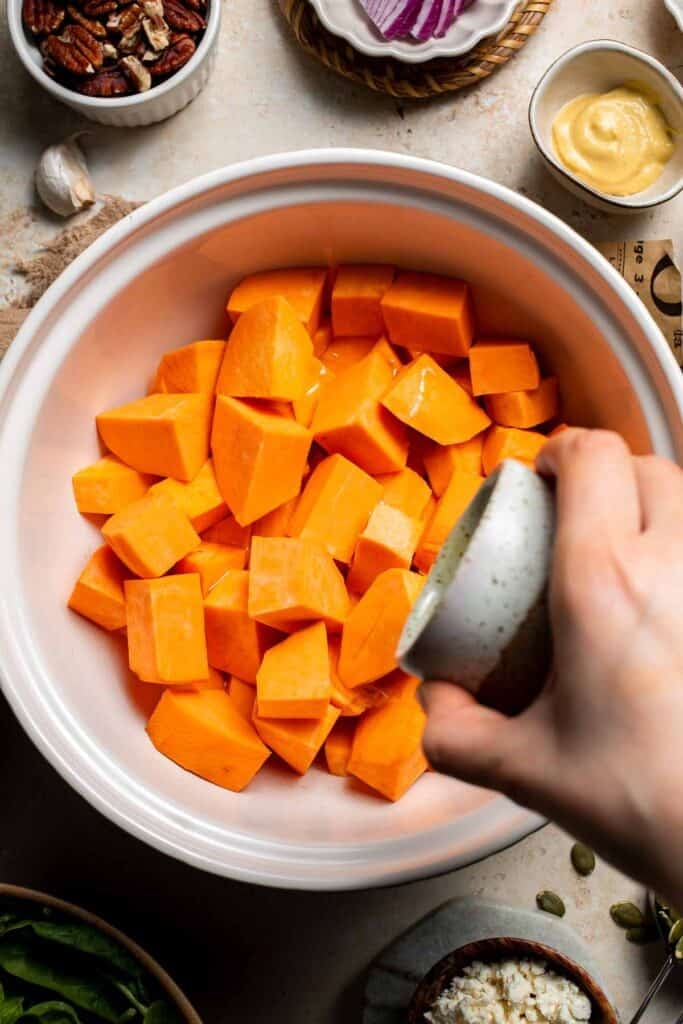 Adding olive oil to diced sweet potatoes in a bowl