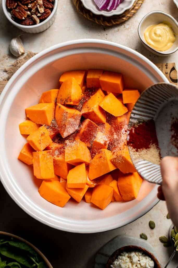 Adding spices to diced sweet potatoes in a bowl