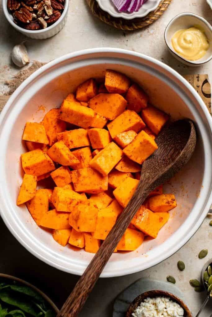 Seasoned diced sweet potatoes being tossed with a wooden spoon in a bowl