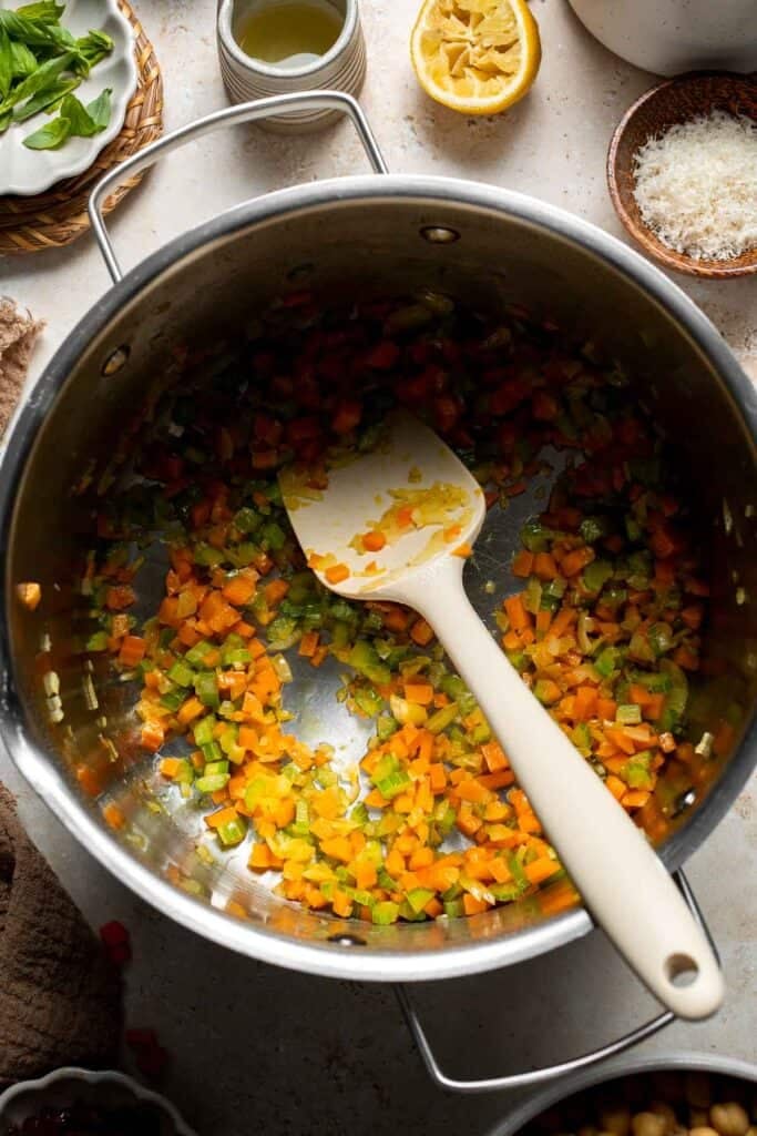 Sautéed vegetables being stirred in a pot with a silicone spoon