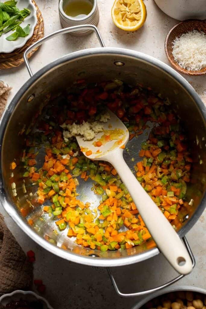 Minced garlic being added to sautéed vegetables in a pot