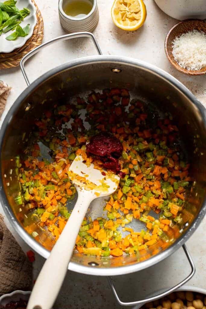 Tomato paste being stirred into sautéed vegetables in a pot
