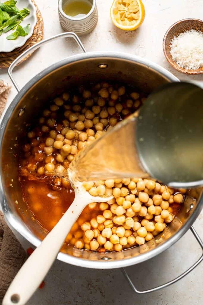 Vegetable broth being poured into a pot of chickpeas and vegetables